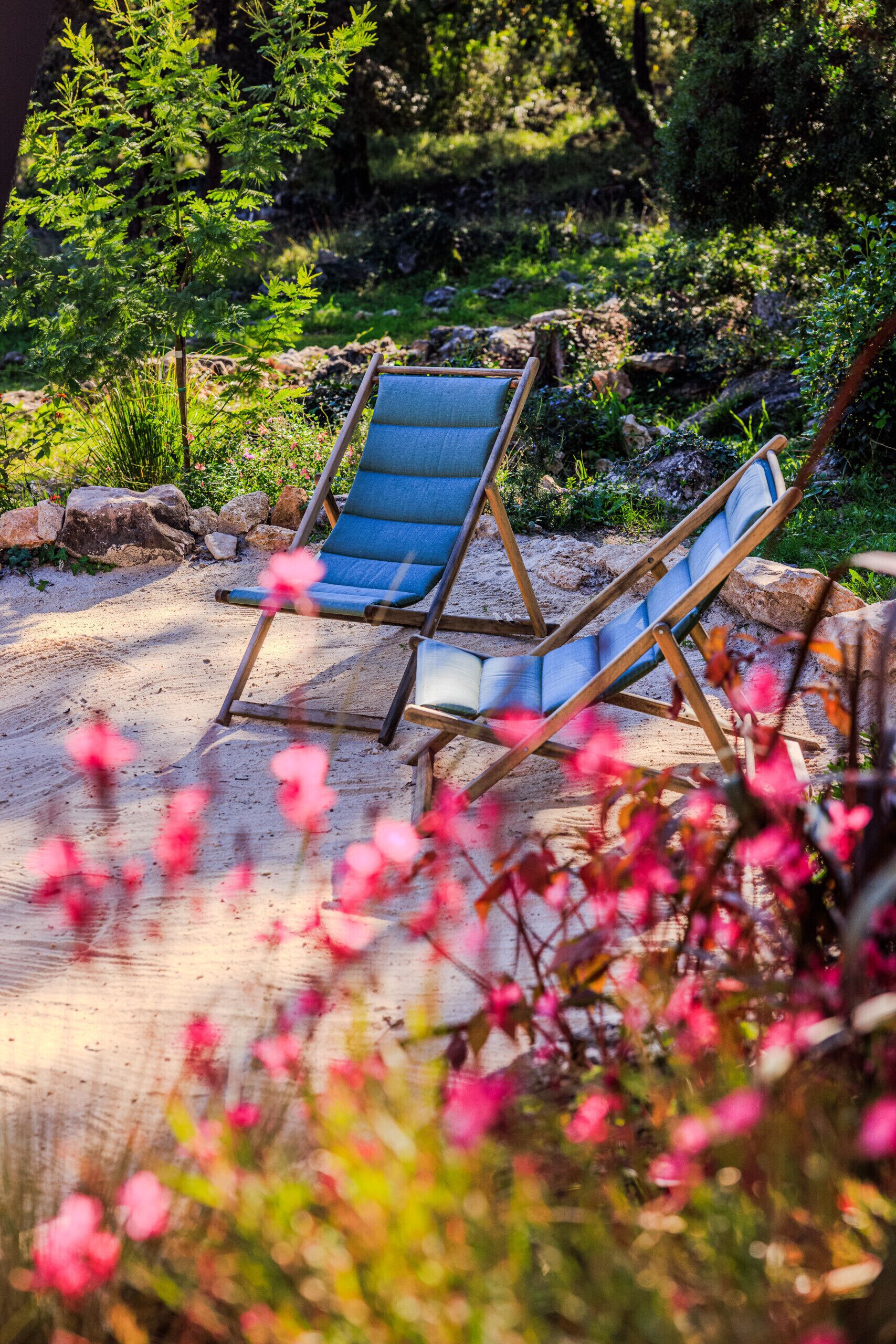 Two blue lounge chairs in a garden setting with rocks and greenery.