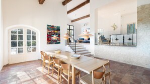 Un'ampia sala da pranzo con un tavolo e sedie in legno, una scala che conduce a un livello superiore e un'ampia finestra che permette alla luce naturale di illuminare l'ambiente.