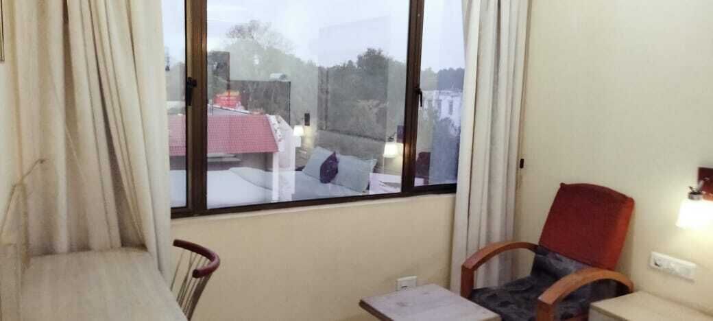 Habitación de hotel con un ventanal grande, una silla, una mesita y un aplique de pared.