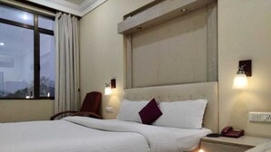 A hotel room with a bed, a nightstand, a lamp, and a window with curtains. - THE RASS HOTEL (Kanpur)