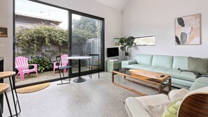 Una sala de estar moderna con un gran ventanal corredera que da a un jardín, un sofá verde claro, una mesa de centro de madera y sillas rosas.