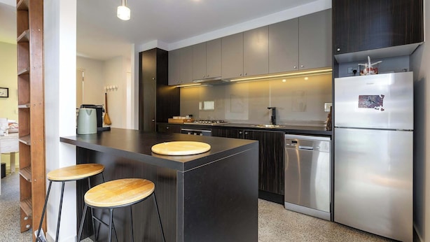 Una cocina moderna con una isla central, electrodomésticos de acero inoxidable y taburetes de madera.