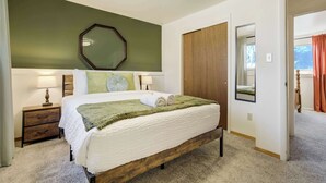 A neatly arranged bedroom with a bed, bedside tables, a mirror, and a door leading to another room. - Trailbend Crossing! Hot Tub near Garden of the Gods (Colorado Springs)