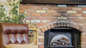 A leather armchair with a matching ottoman, a woven basket, and a fireplace with a brick wall and a mirror above it. - Trailbend Crossing! Hot Tub near Garden of the Gods (Colorado Springs)