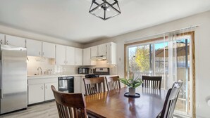 A modern kitchen with white cabinets, a wooden dining table, and a potted plant. - Trailbend Crossing! Hot Tub near Garden of the Gods (Colorado Springs)
