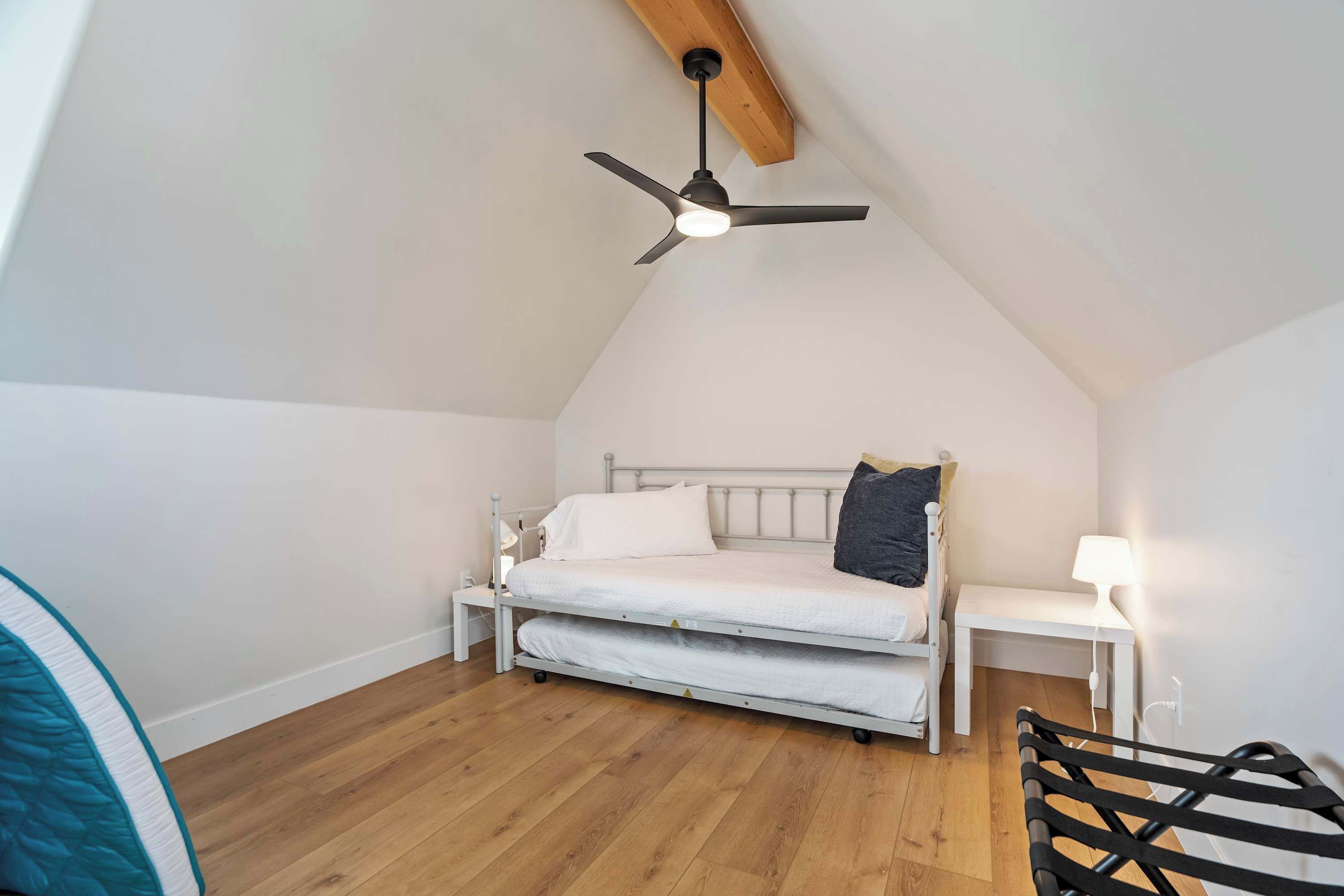 A small, cozy bedroom with a single bed, a bedside table with a lamp, and a ceiling fan.