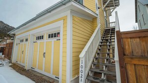 A yellow building with a white exterior, a wooden staircase, and a garage with a red sign.