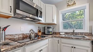 Uma cozinha com armários brancos, bancada de granito, coifa de aço inoxidável, micro-ondas, torradeira e janela com vista para o verde.