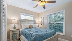 Quarto com cama, luminárias de cabeceira, ventoinha no teto e janela com persianas.
