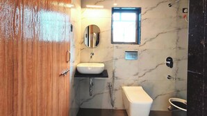 A modern bathroom with a wooden door, a white sink, a toilet, and a mirror. - Hotel Satkar Inn (Khalapur)