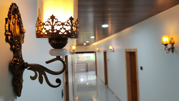 A hallway with ornate wall sconces, a polished floor, and doors at the end. - Hotel Satkar Inn (Khalapur)