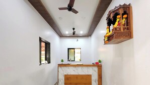 A reception area with a marble counter, ceiling fan, and decorative shelf with flowers. - Hotel Satkar Inn (Khalapur)