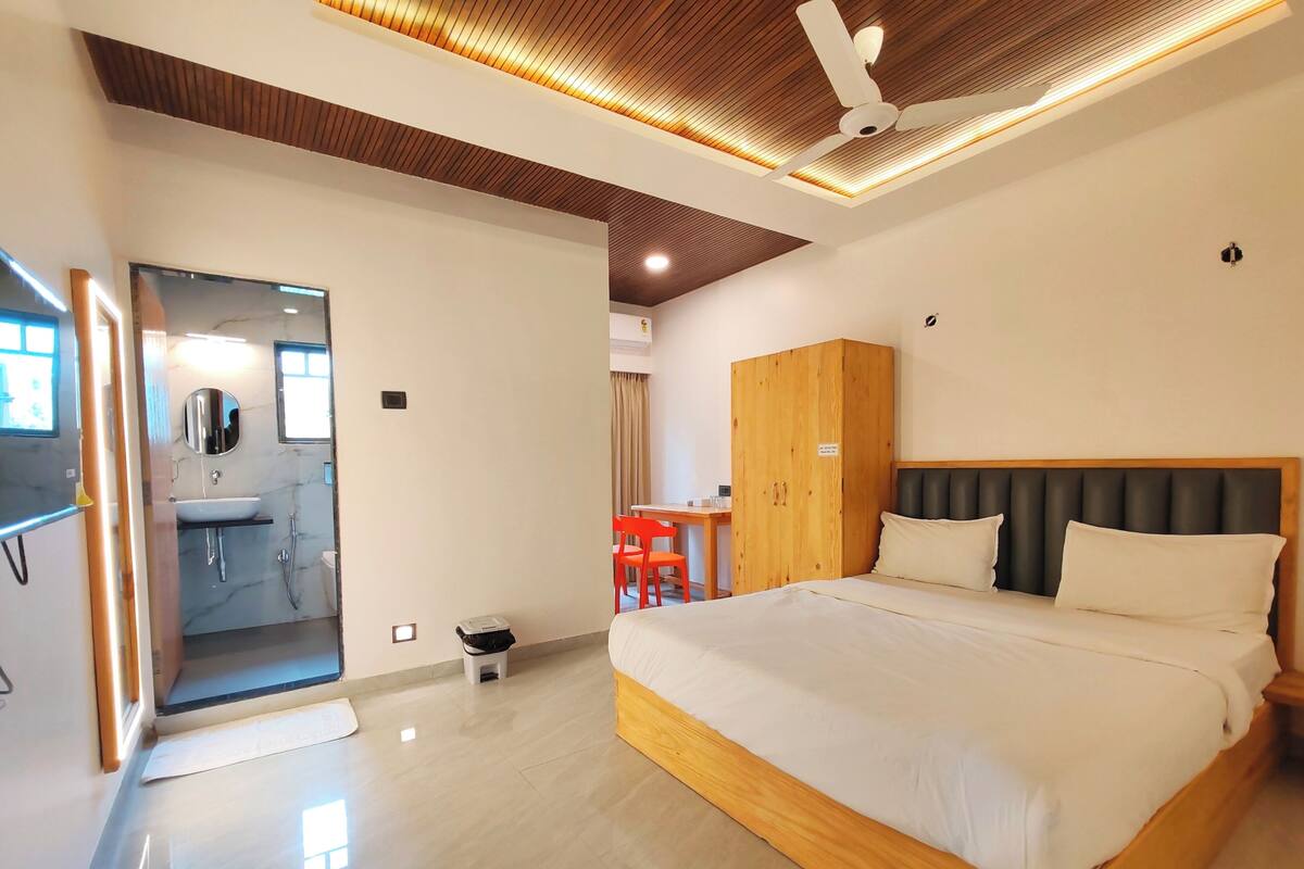 A modern hotel room with a large bed, wooden wardrobe, and a bathroom with a mirror and sink.