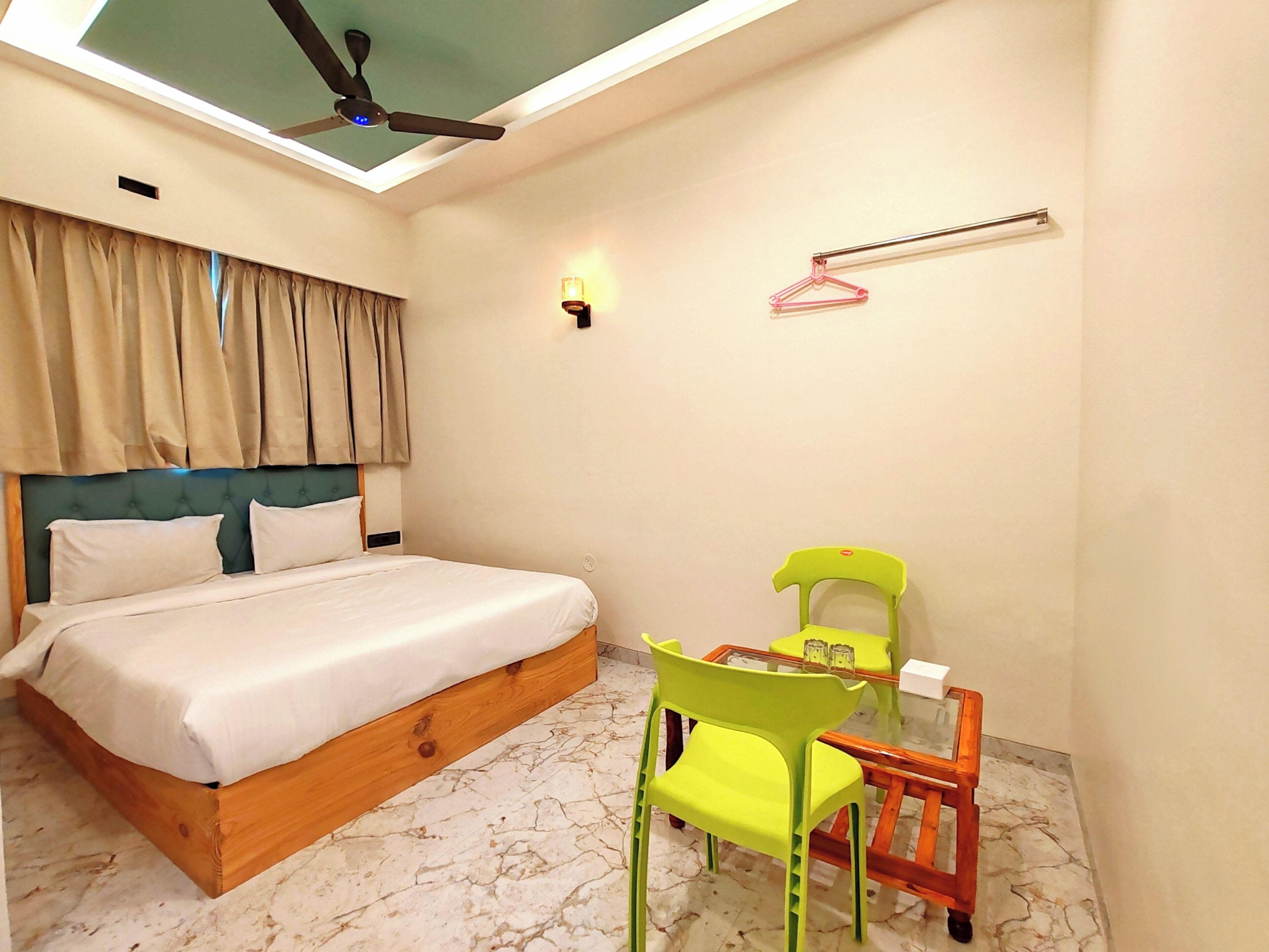 Un dormitorio con cama, ventilador de techo, mesa con sillas y perchero en la pared.
