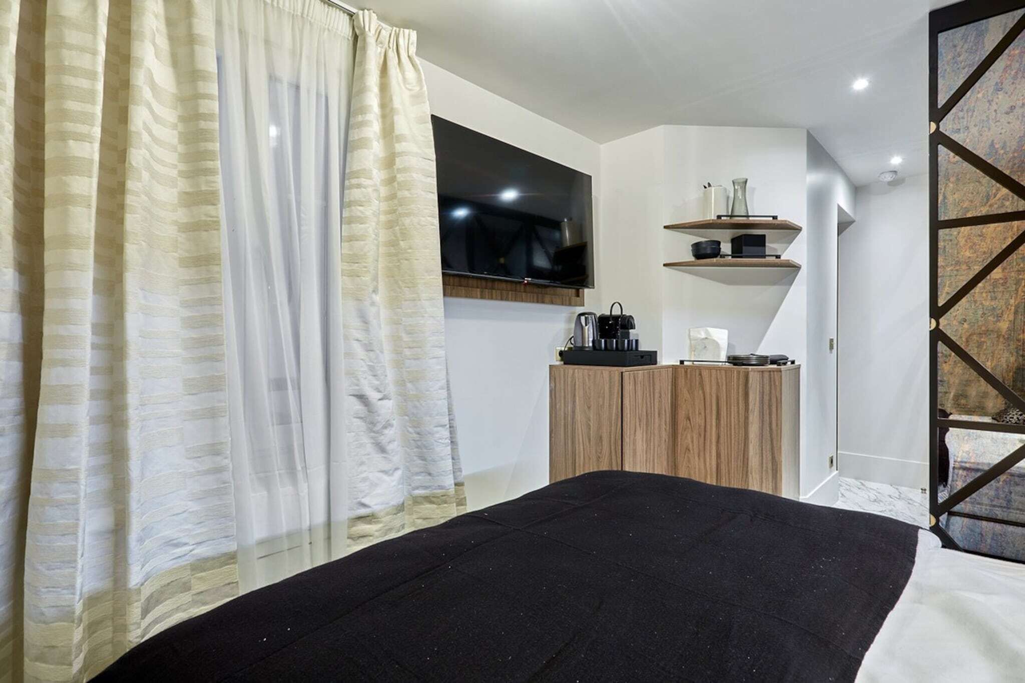 Een moderne slaapkamer met een bed, een aan de muur bevestigde televisie en een houten kast met een plank erboven.