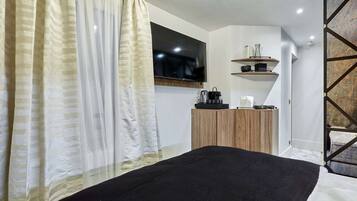 Een moderne slaapkamer met een bed, een aan de muur bevestigde televisie en een houten kast met een plank erboven.