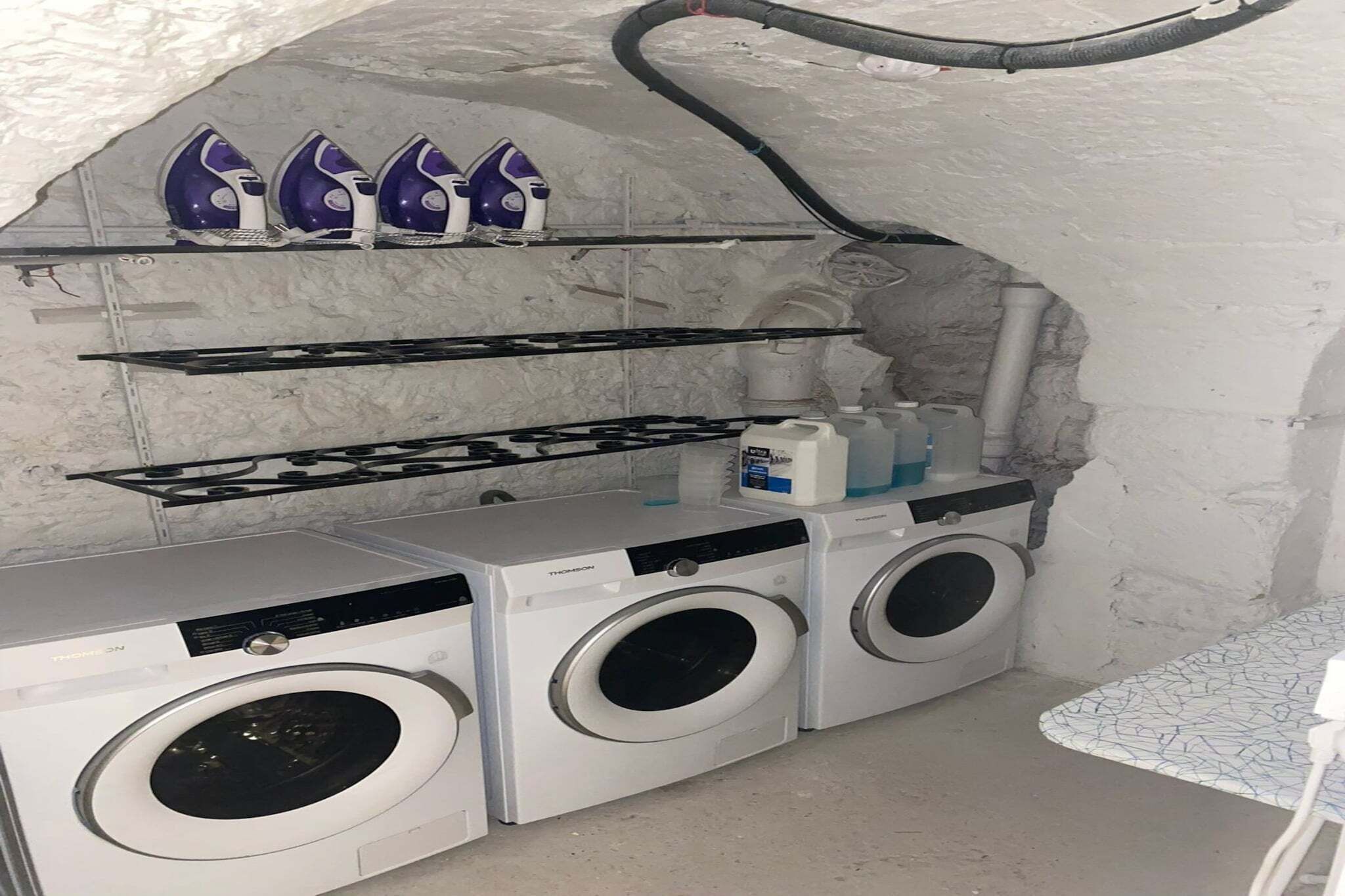 Un espace buanderie compact comprenant un lave-linge, un sèche-linge et une étagère où sont rangés les produits de nettoyage.