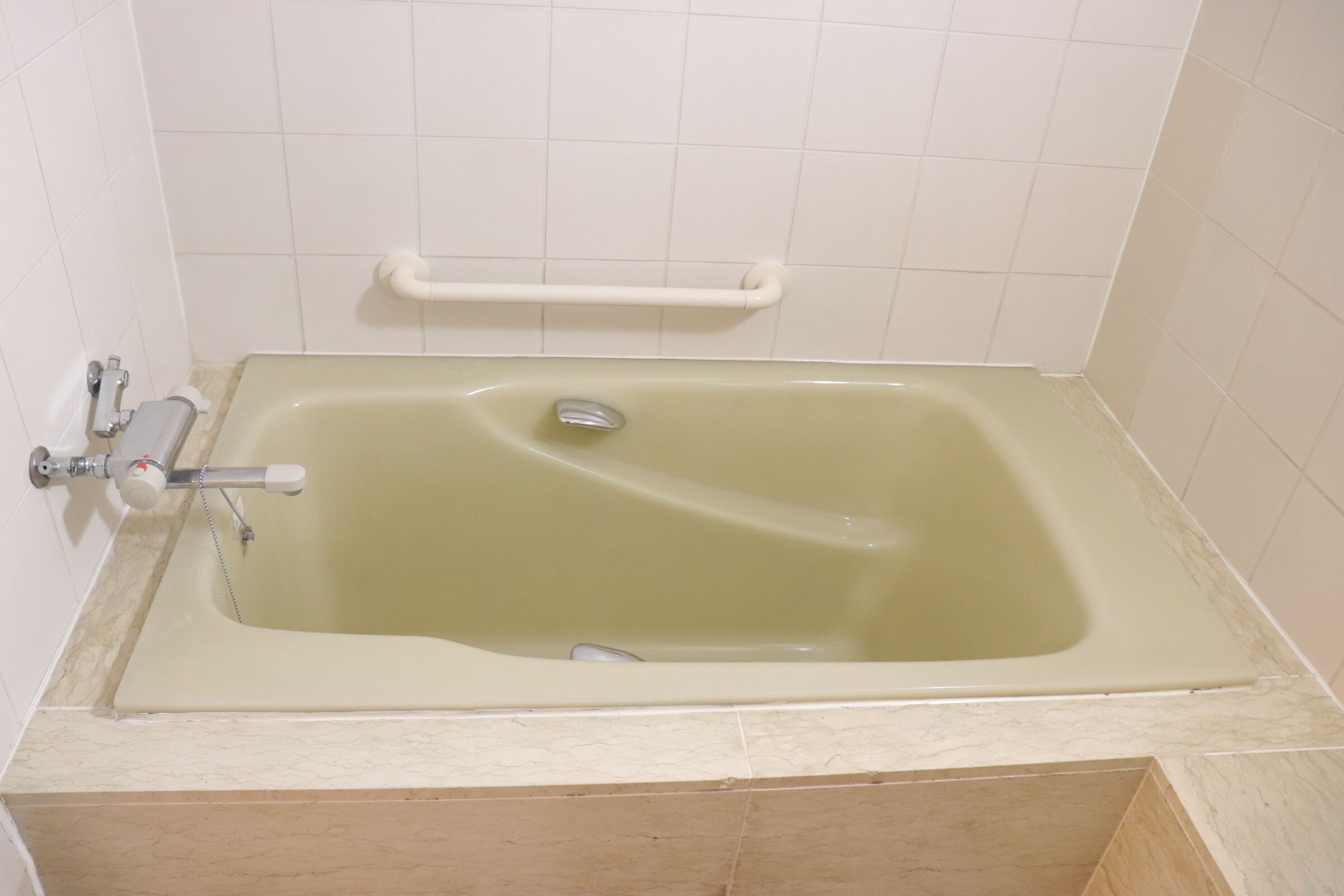 A standard bathtub with a grab bar, a faucet, and a control valve.