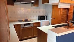 A compact kitchen with wooden cabinets, a microwave, a dishwasher, and a built-in oven. - Maison Odori Park (Sapporo)