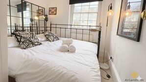 Ein Schlafzimmer mit einem Bett, einem schwarzen Metall-Kopfstück, einem Fenster mit schwarzem Vorhang und einer wandmontierten Leuchte.