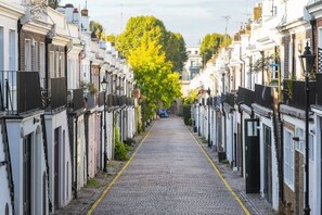 Eine enge Kopfsteinpflasterstraße, gesäumt von weißen Gebäuden, von denen jedes ein schwarzes Tor und einen kleinen Garten besitzt.