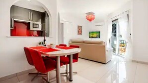 A modern living room with a beige sofa, a dining area with red chairs, and a kitchen with white cabinets. - Gorgeous Apartment in Paradise Complex (Paphos)