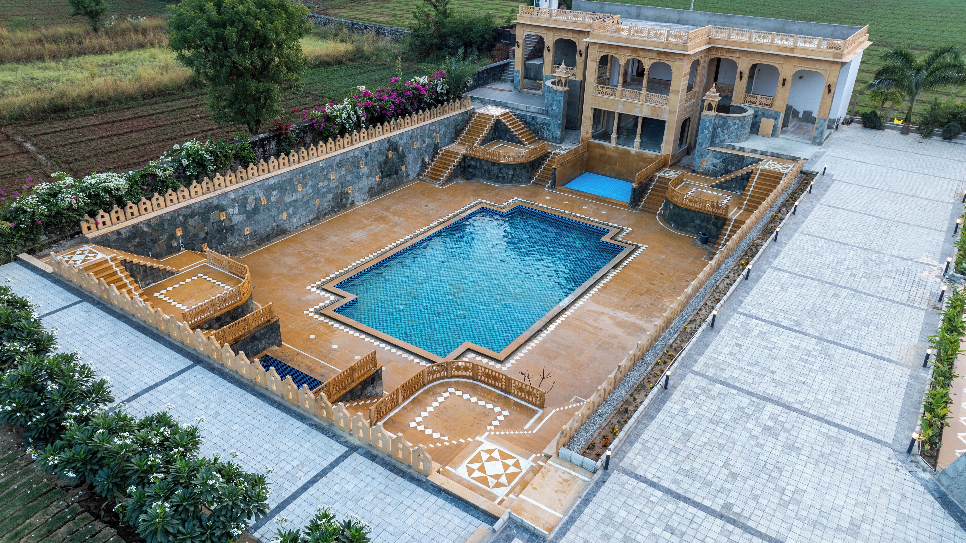 Una piscina grande y cuadrada con un diseño geométrico de mosaicos, rodeada por un muro de piedra con detalles intrincados.