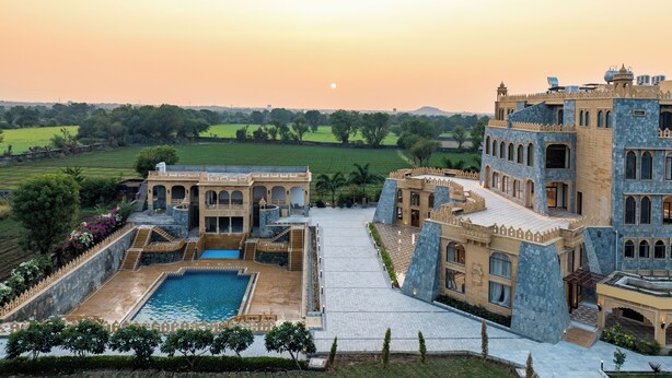 A large, historic building with a swimming pool, surrounded by lush greenery and fields. - Raj Leela Heritage Resort by Estherea (Ghanerao)