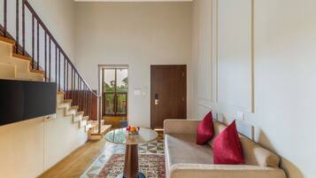 Una sala de estar moderna con una escalera, un sofá con cojines rojos, una mesa redonda con fruta y un televisor montado en la pared.