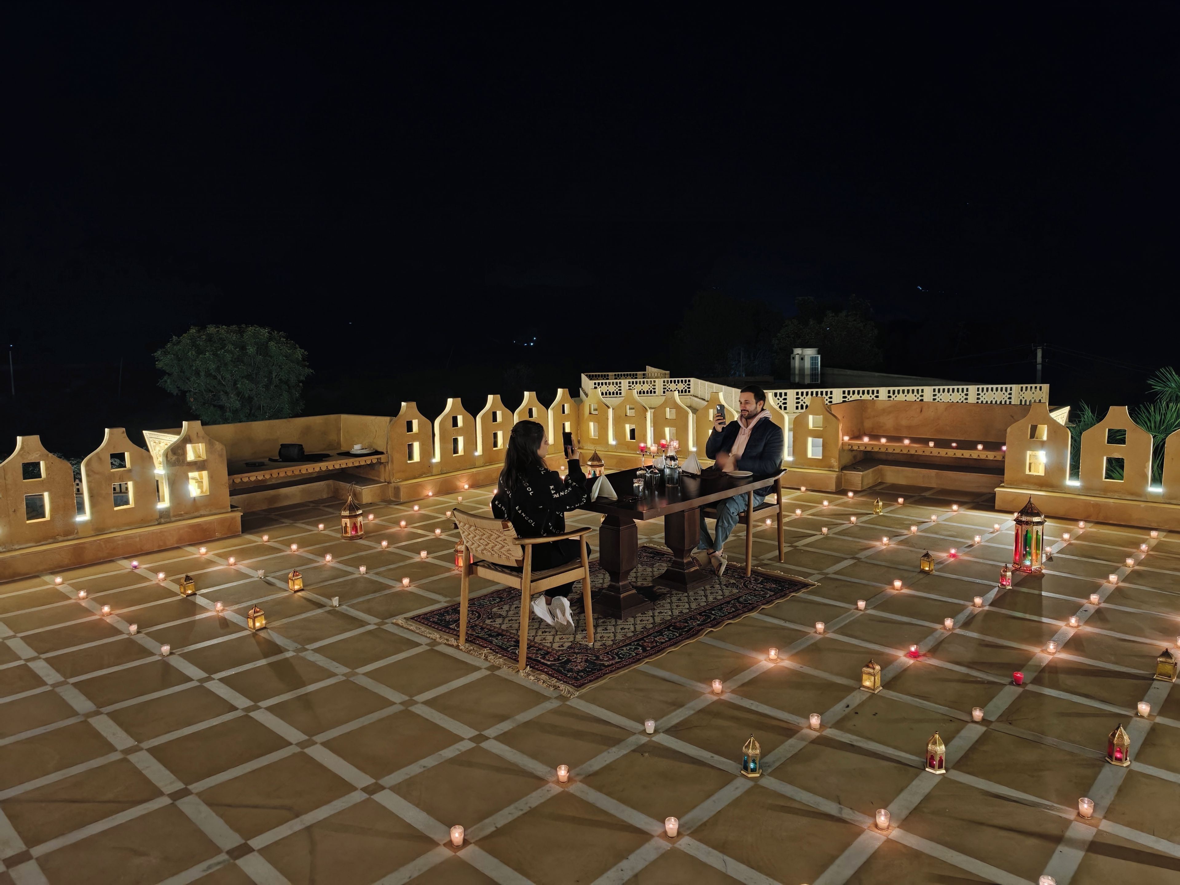 A rooftop terrace with a checkered floor, a table with chairs, and a decorative railing.