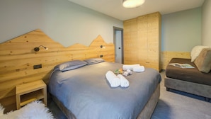 A bedroom with a large bed, a smaller sofa, wooden paneling on the walls, and a ceiling light. - Loredana 2 (Livigno)