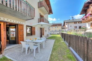 A courtyard with a table and chairs, a wooden fence, and a building with balconies. - Loredana 2 (Livigno)