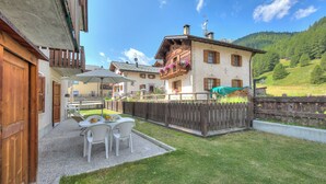 A courtyard with a table and chairs, a wooden fence, and a building with balconies. - Loredana 2 (Livigno)