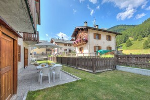 A courtyard with a table and chairs, a wooden fence, and a building with balconies. - Loredana 2 (Livigno)