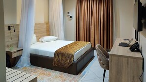 Een hotelkamer met een bed, een bureau, een stoel, een televisie en gordijnen.