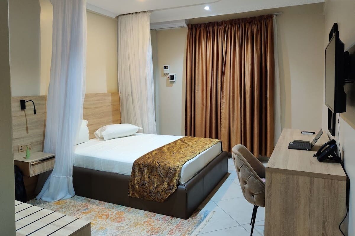 A hotel room with a bed, a desk, a chair, a television, and curtains.