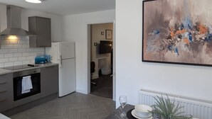 A modern kitchen with grey cabinetry, a built-in oven, and a blue coffee machine. There is a dining area with a table set for two, a vase with greenery, and a large abstract painting on the wall. - 4 BR House | Unli Parking | Bathtub (West Midlands)