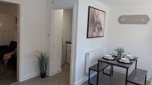 A dining area with a table set for four, a potted plant, and a 'Be our guest' sign on the wall. - 4 BR House | Unli Parking | Bathtub (West Midlands)