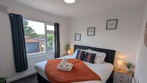 A hotel room with a bed, a bedside table with a lamp, a window with curtains, and a view of the outside. - 4 BR House | Unli Parking | Bathtub (West Midlands)