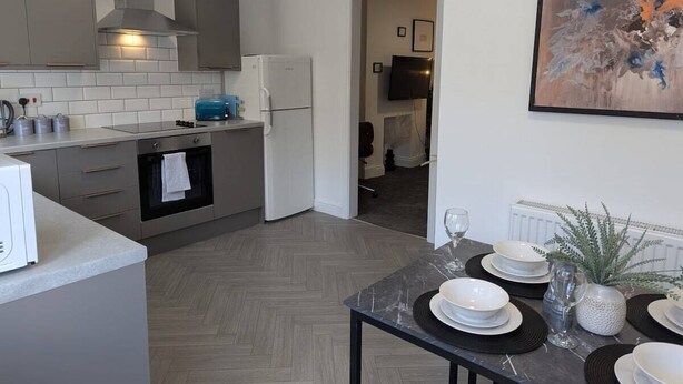 A modern kitchen with grey cabinets, a built-in oven, and a dining area with a table set for four. - 4 BR House | Unli Parking | Bathtub (West Midlands)