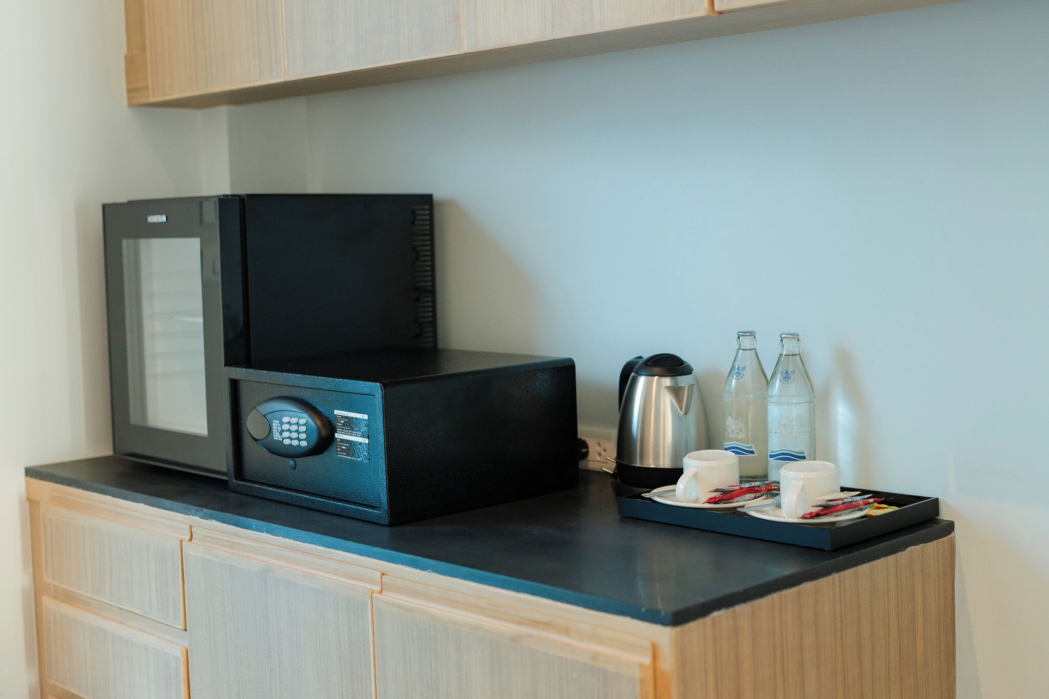 A microwave and coffee maker on a kitchen counter with a tray of cups and bottles.