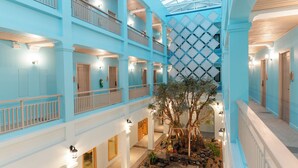 Un atrium d’hôtel à plusieurs niveaux, doté de balcons, d’un arbre central et d’un mur orné de motifs.