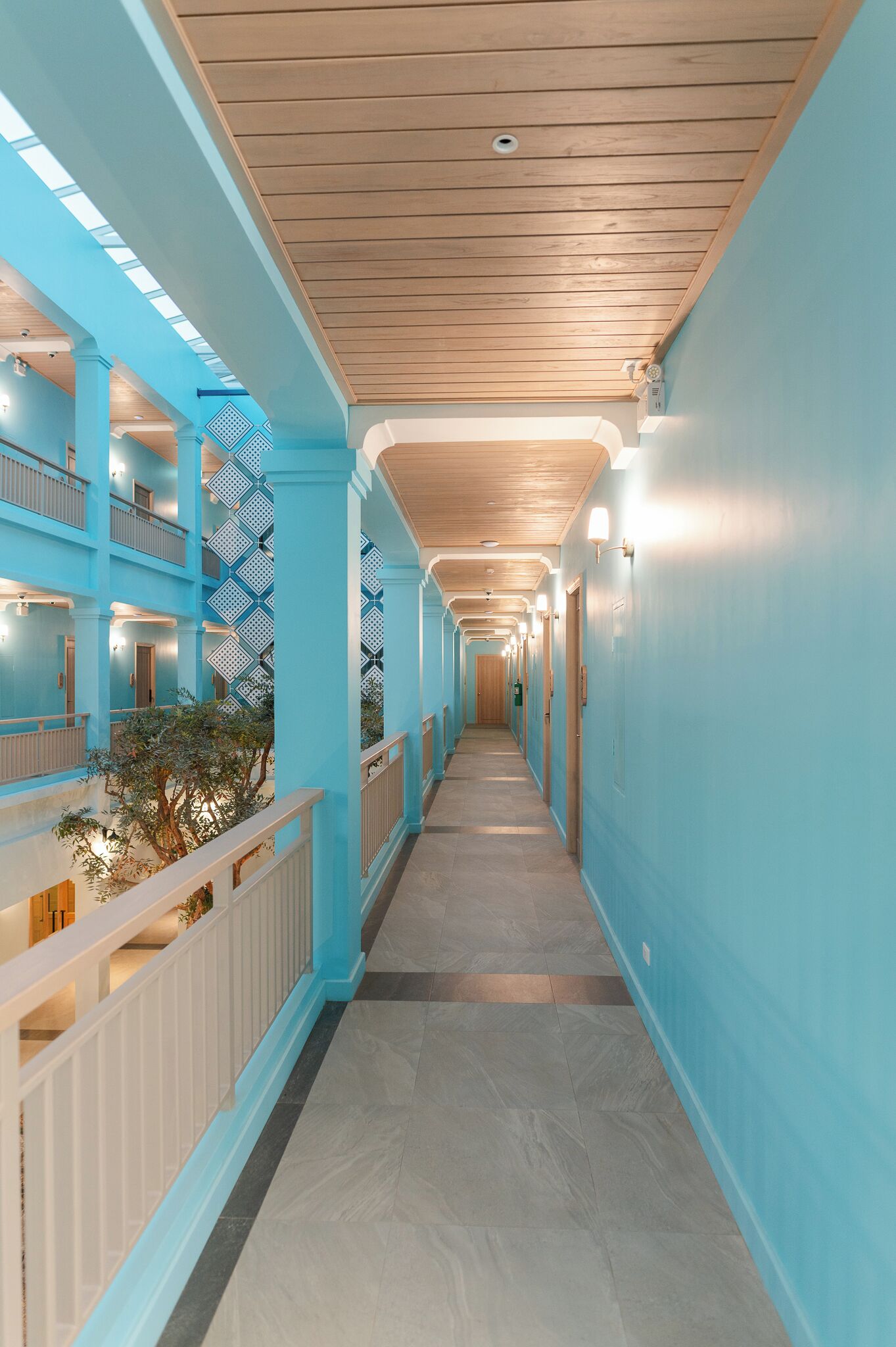 A long corridor with wooden ceilings and light blue walls, leading to multiple balconies and rooms.