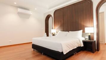 Quarto de hotel moderno com uma cama grande, cabeceira de madeira, duas mesas de cabeceira com luminárias e um aparelho de ar condicionado na parede.