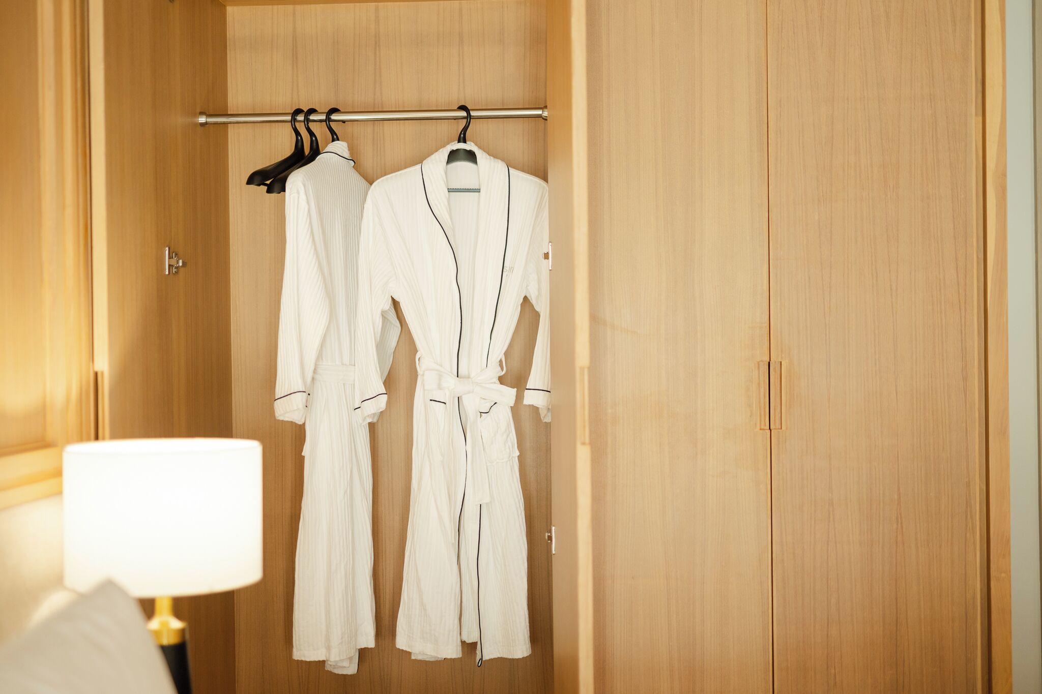 A wooden wardrobe with two white robes hanging on a rod.