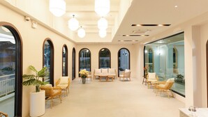 Un hall d’entrée spacieux avec un plafond haut, de grandes fenêtres et un coin salon agrémenté de fauteuils en osier et d’un canapé.