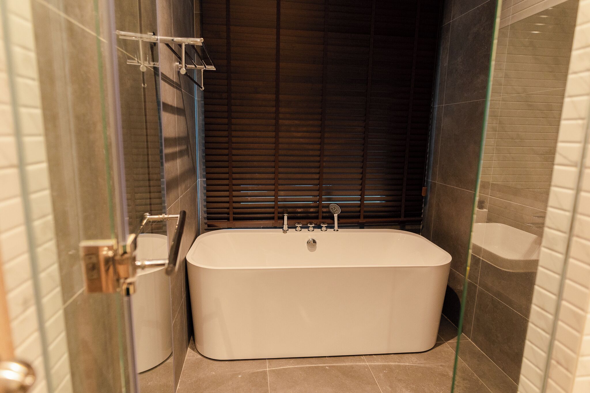Een moderne badkamer met een vrijstaand bad, een douchecabine met glazen wanden en een donkere houten achtergrond.