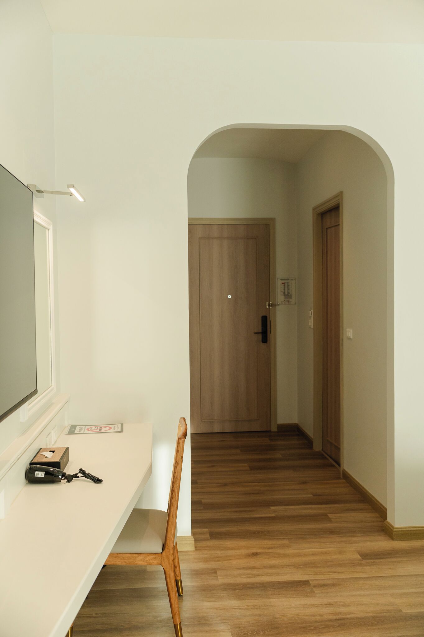 Un pasillo con suelo de madera, pared blanca y una puerta al final.