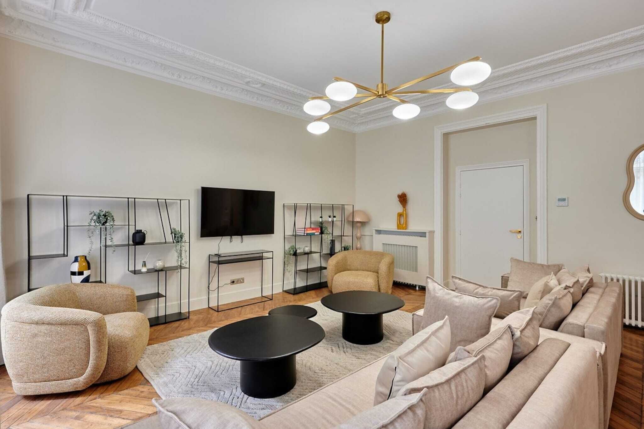 Een moderne woonkamer met een bank, twee zwarte salontafels, een televisie en een decoratieve plafondlamp.