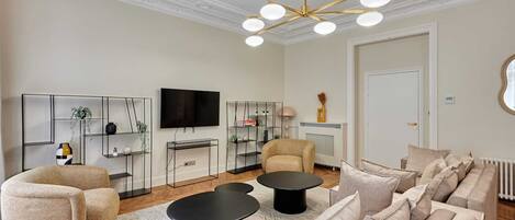Een moderne woonkamer met een bank, twee zwarte salontafels, een televisie en een decoratieve plafondlamp.